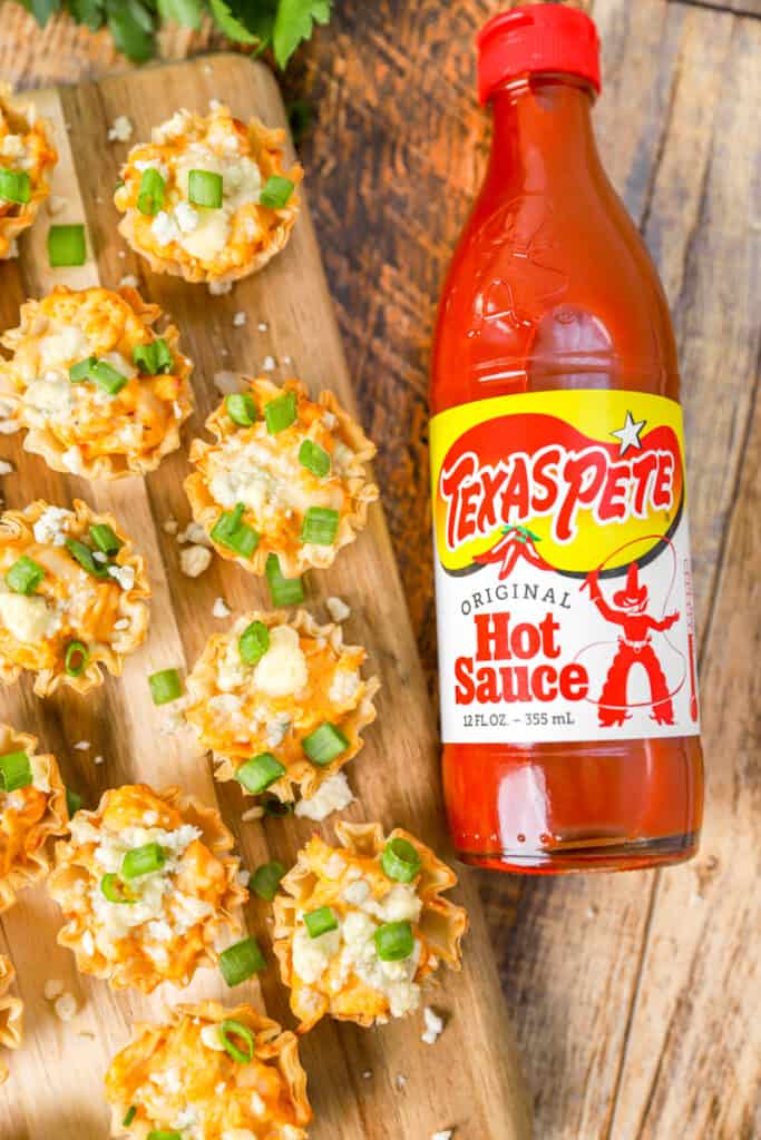 overhead shot of the buffalo chicken bites on a wood cutting board with a bottle of hot sauce.