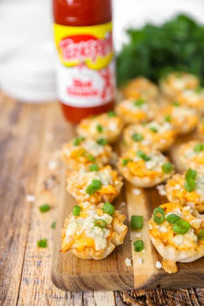 buffalo chicken bites on a wood cutting board, in the background a bottle of hot sauce, plates, and parsley