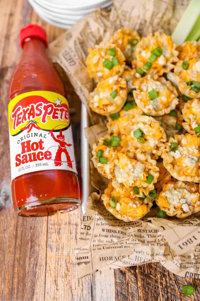 overhead shot of the bites on a platter on a wood surface with the bottle of hot sauce.