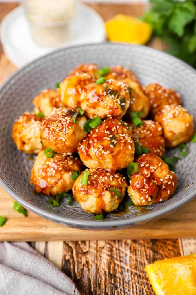 closer shot of the orange chicken meatballs in a grey bowl topped with scallions and sesame seeds.