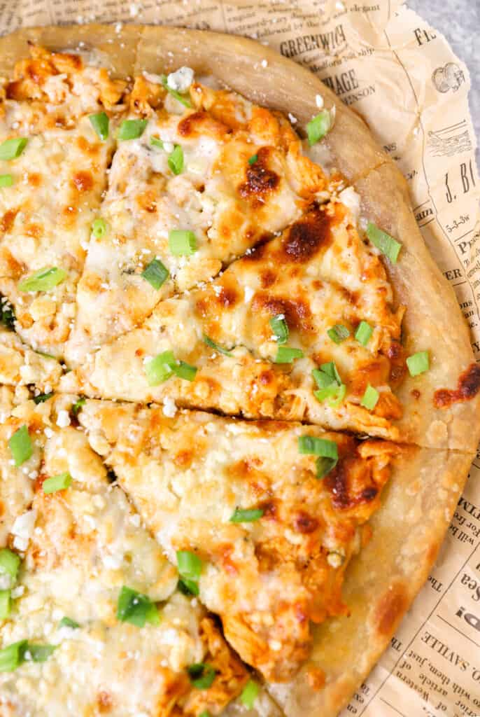 close shot of the slices of the pizza topped with diced scallions on brown newsprint paper.