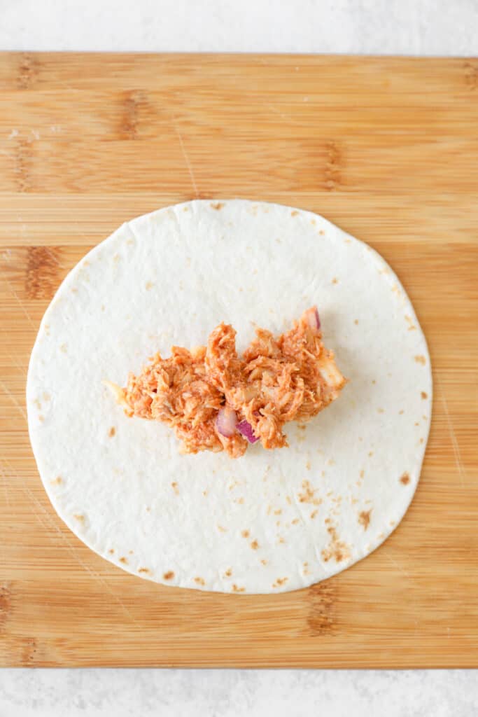 overhead view of the flour tortilla filled with the bbq chicken mixture on a wood board.