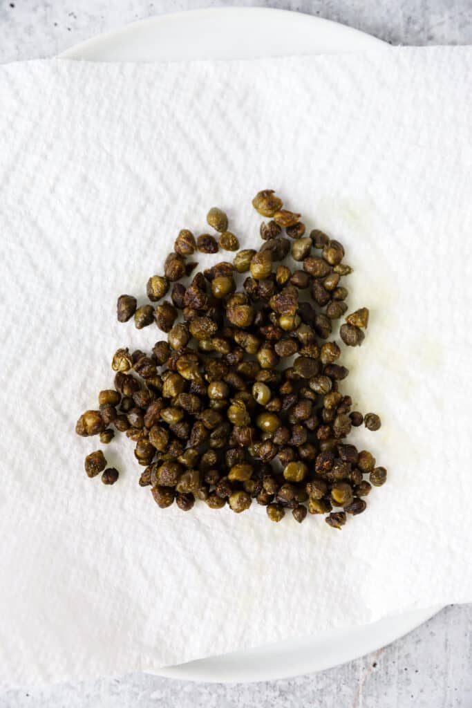 fried capers drying on a paper towel lined plate.