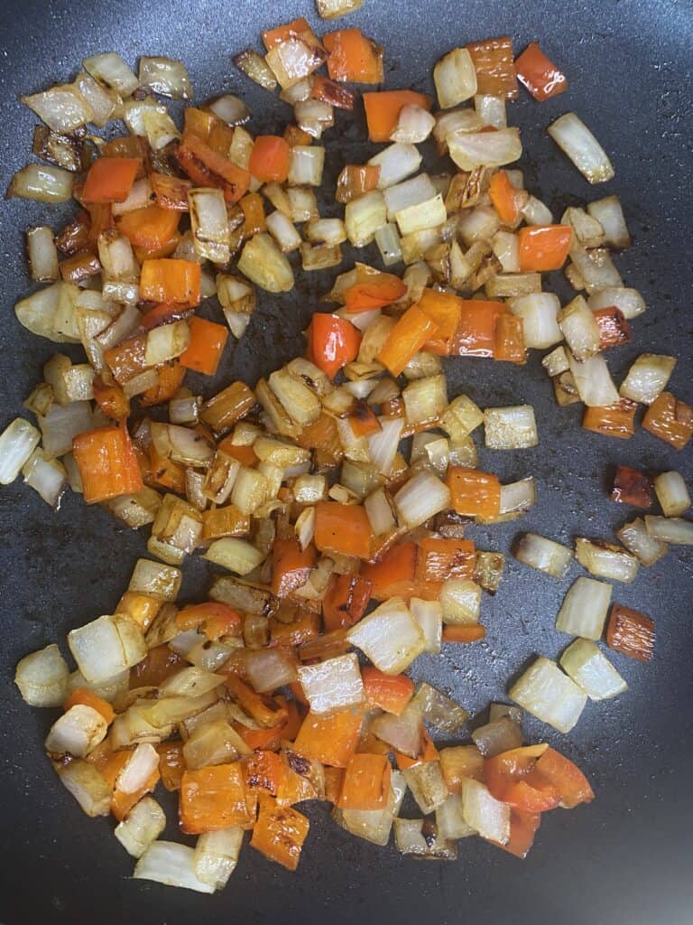 overhead shot of the white onions and red peppers in a pan.