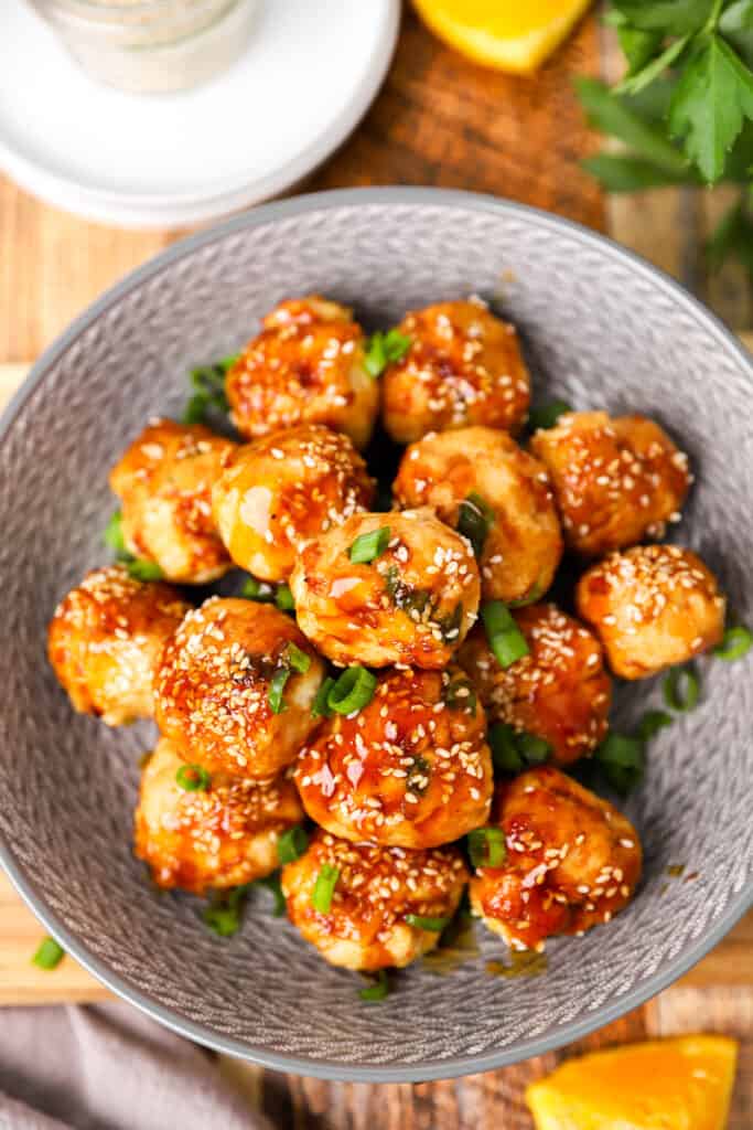 overhead shot of orange teriyaki chicken meatballs in a grey bowl on a wood board.