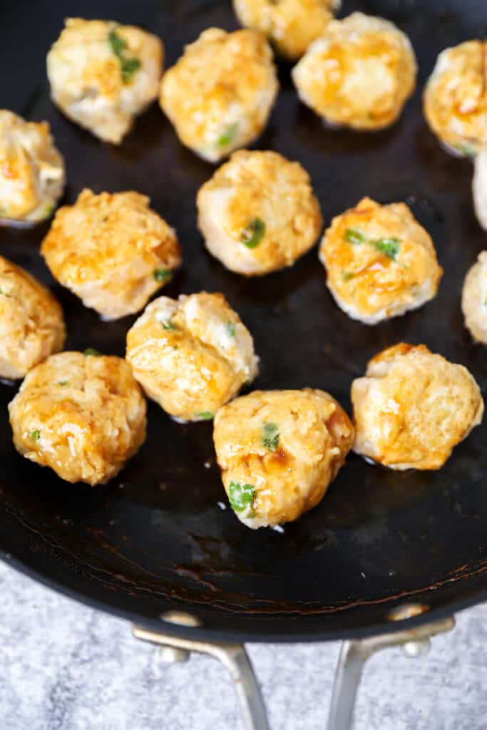 the chicken meatballs being browned in a black non-stick pan.