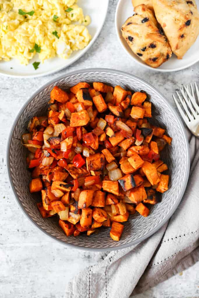 overhead shot of sweet potato home fries in a grey bowl. Eggs and scones off to the upper left of right corners