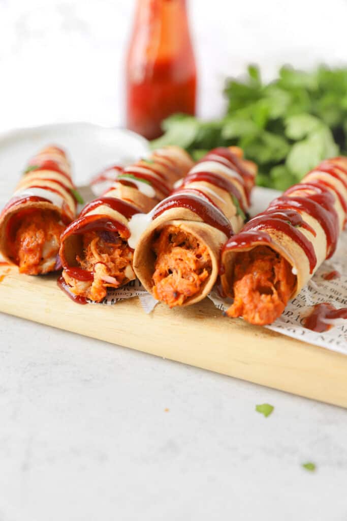 side view into the taquitos showing the mixture. bottle of bbq sauce and parsley in the back.