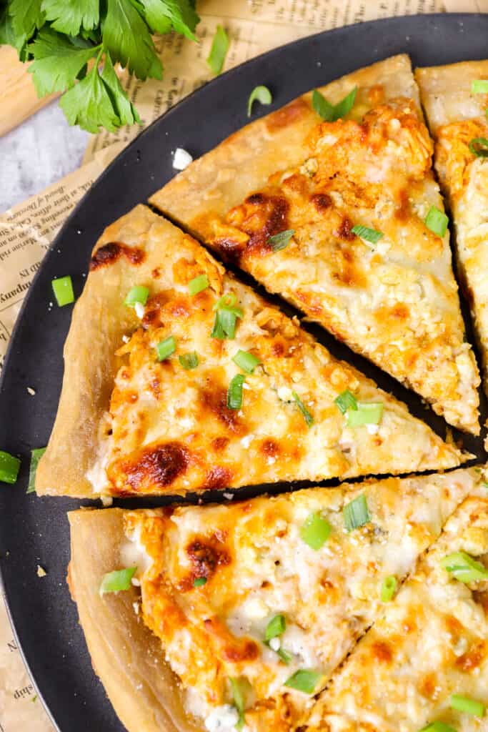 angled photo of the pizza slices on the pizza pan with parsley in the background.