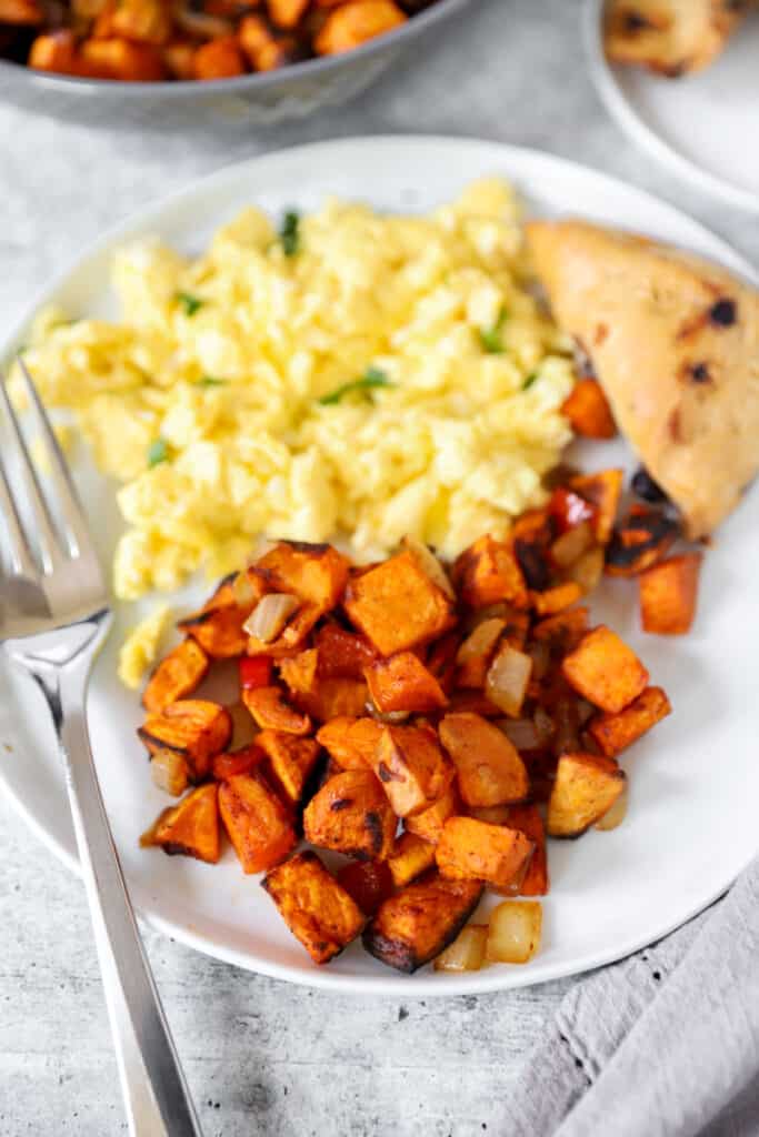 a plate with scrambled eggs, a blueberry scone, and the sweet potato home fries with a fork.