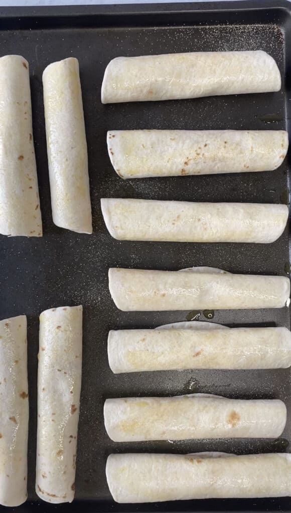 overhead view of the rolled flour taquitos on a baking sheet.