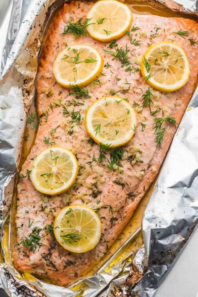 overhead shot of a large salmon filet covered in dill and lemon slices in foil.