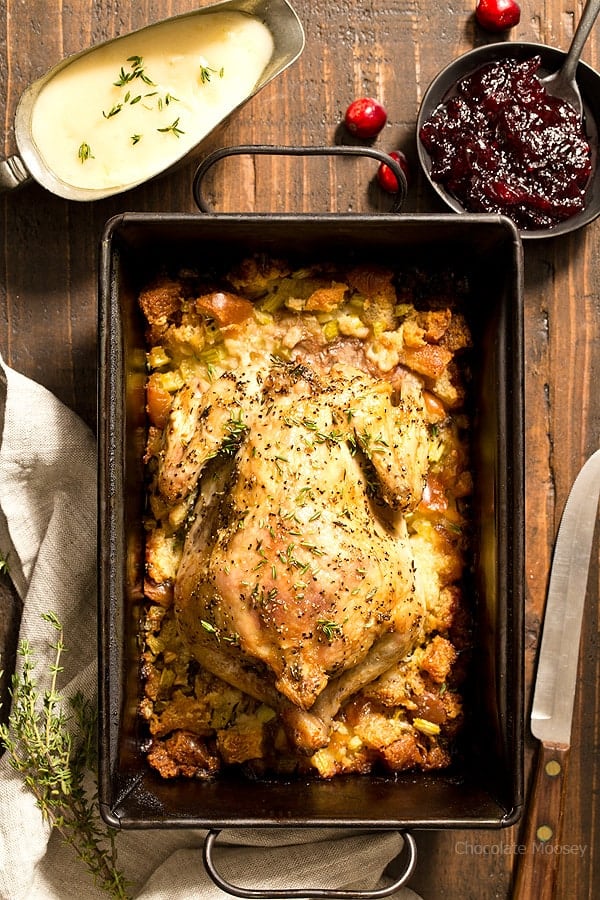 overhead shot of the cornish hen in a baking dish with stuffing on a wood surface.