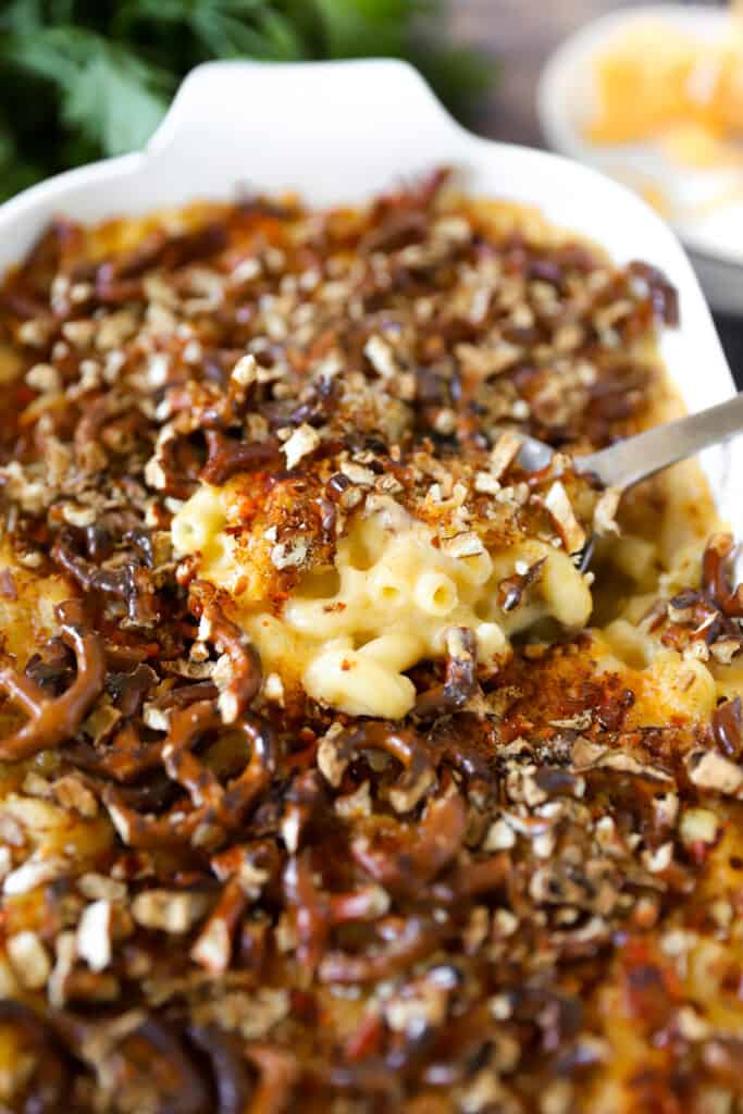 silver serving spoon scooping the mac and cheese from a white casserole dish.