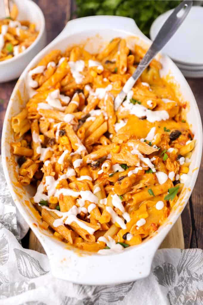 angled shot showing the pasta in the casserole dish with a large serving spoon drizzled sour cream.