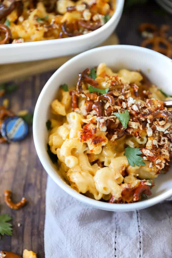 a bowl of beer mac and cheese on a wood surface, a bottle cap from the beer blurred in the back.