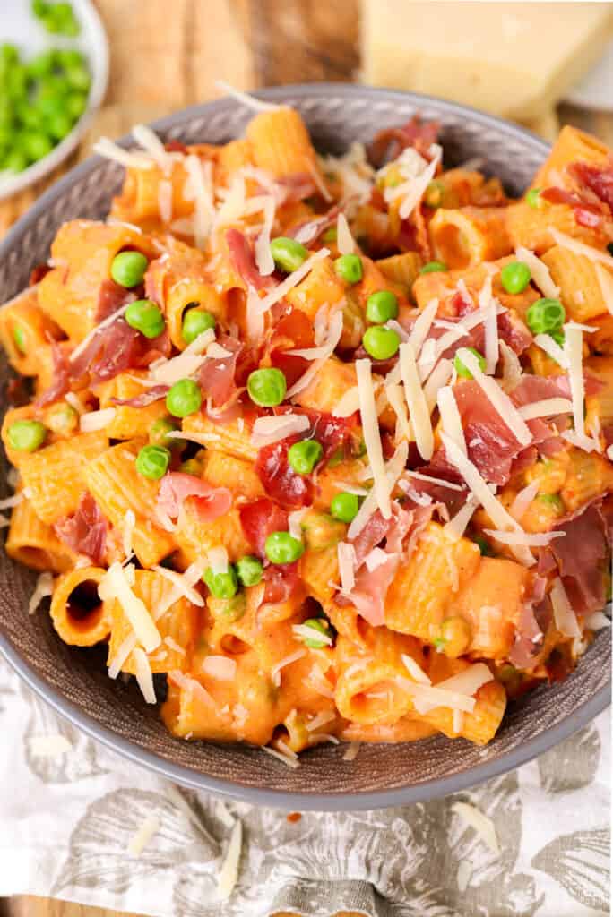 large grey bowl of the rigatoni vodka with peas and crispy prosciutto topped with Parmesan cheese.