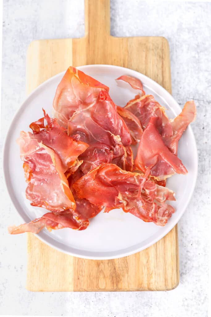 overhead shot of the crispy prosciutto on a plate on a wood cutting board.