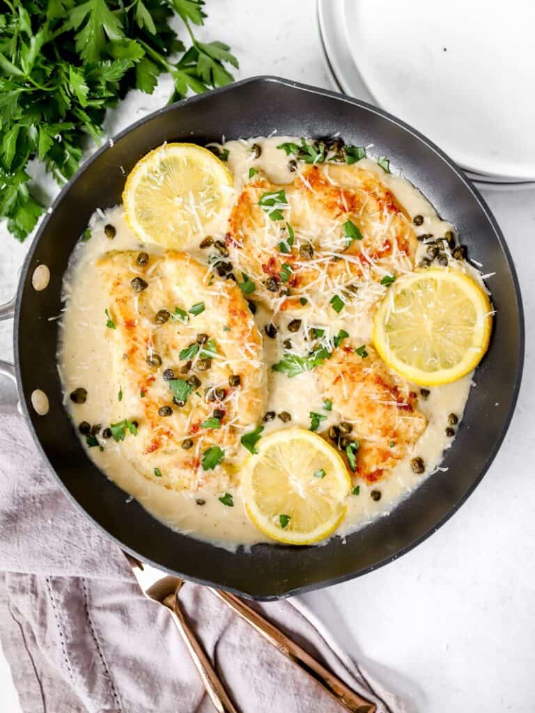 creamy chicken picatta in a black pan with parsley and a grey napkin