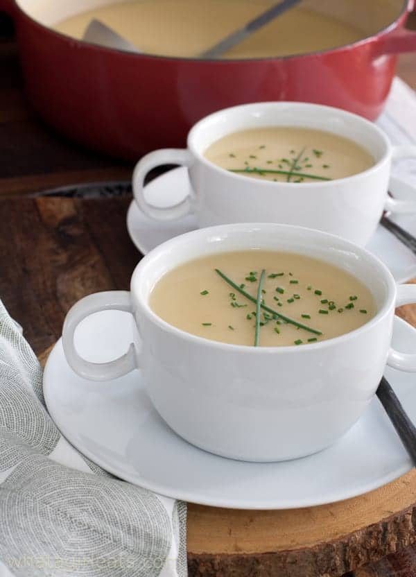 two cups of leek and potato soup on a wood surface.