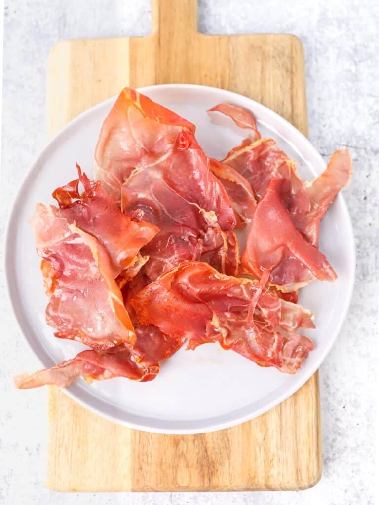 overhead shot of the crispy prosciutto on a white plate on a wood cutting board