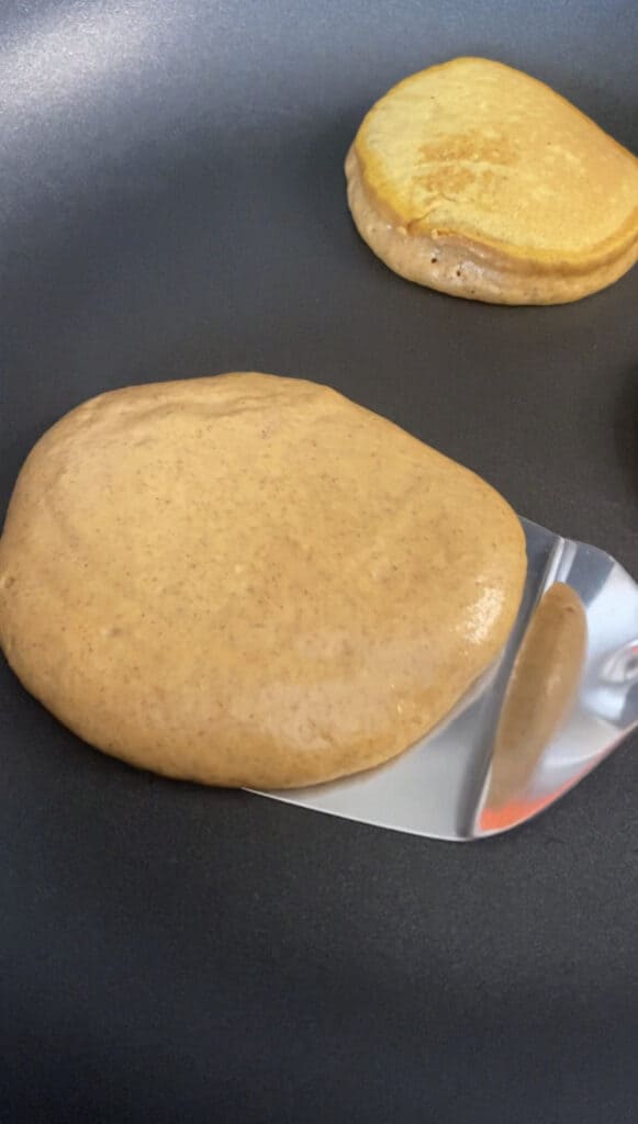 a spatula flipping a pancake in a black non-stick pan