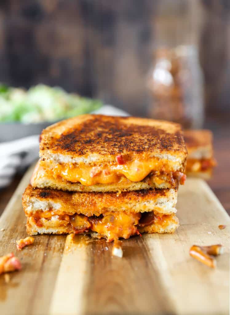 two slices of the pimento cheese grilled cheese stacked on a wood cutting board.