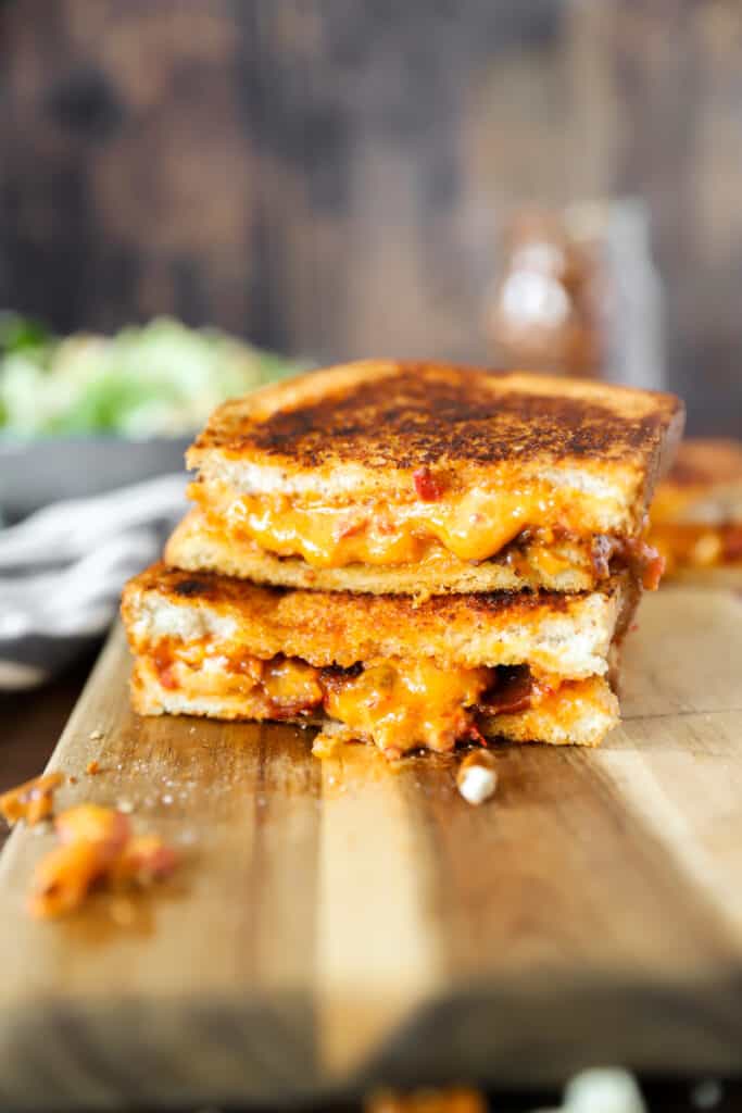 two pieces of the grilled cheese stacked on top of each other on a wood cutting board.