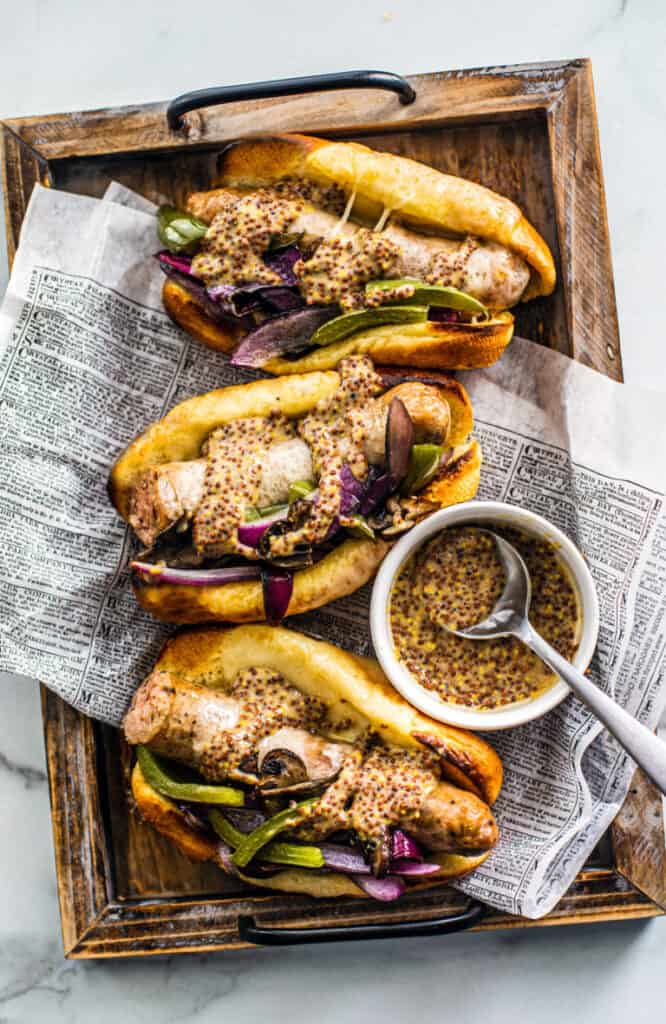 overhead shot of the sausage and pepper sandwiches on newsprint paper and a wood serving tray.