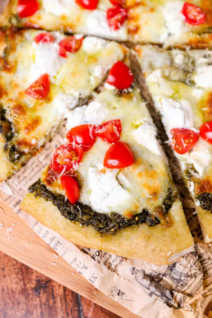 slice of pesto pizza on a wood cutting board.