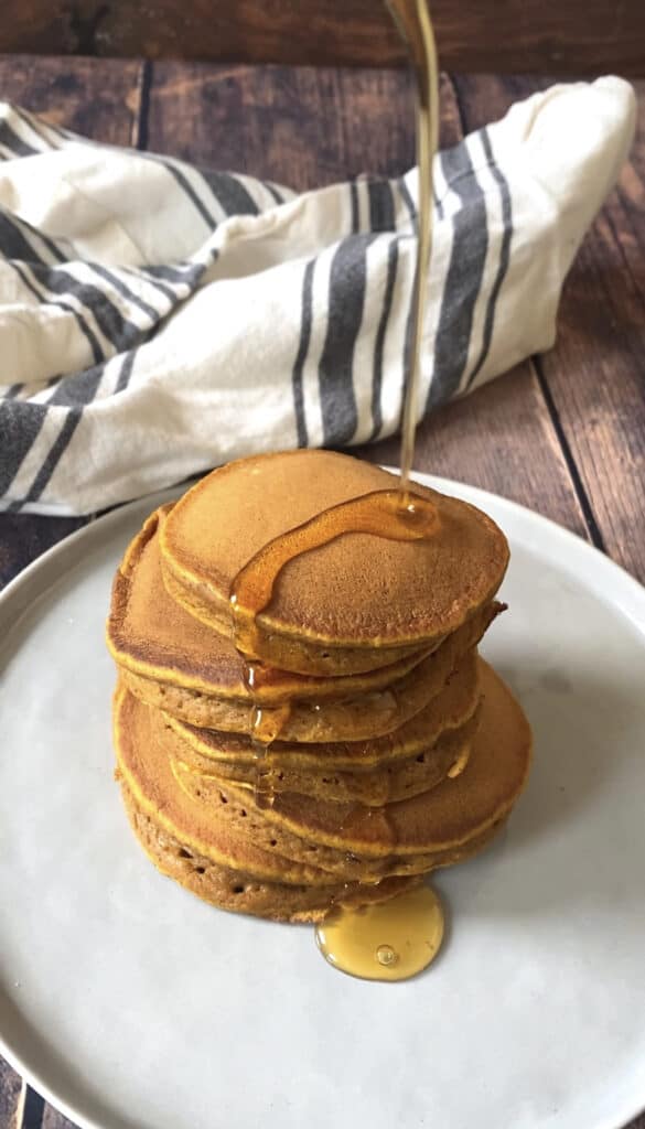 a stack of the pancakes on a wood surface with syrup being drizzle on.