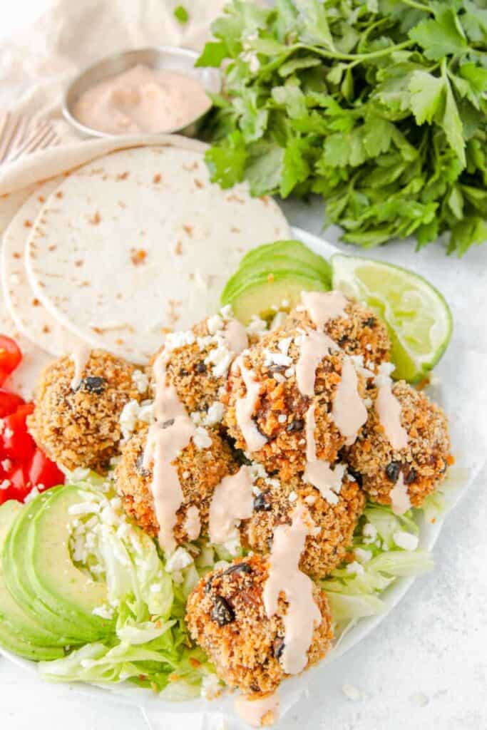 tacos meatballs covered in chipotle sauce on a plate with avocados, lettuce, and tortillas.