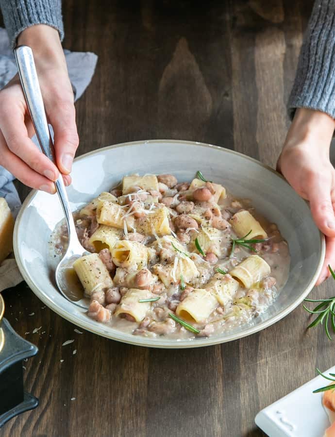 a bowl of pasta e fagioli showing the person's hands holding the spoon.