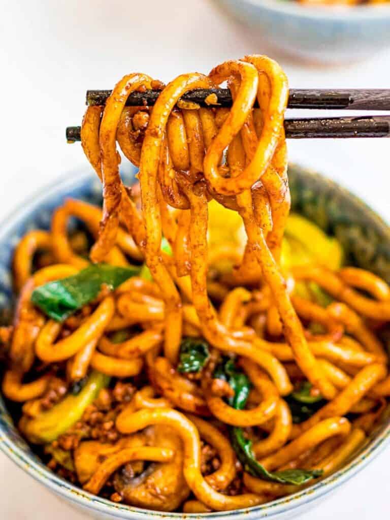 chopsticks holding the noodles above a bowl.