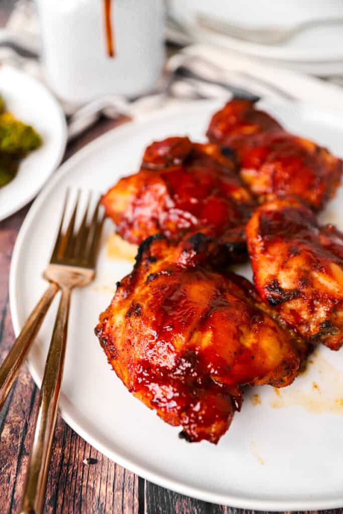 baked BBQ chicken on a white plate with two forks on a wood surface.