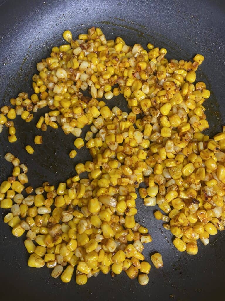 overhead shot of the pan roasted seasoned corn in a black non-stick pan.