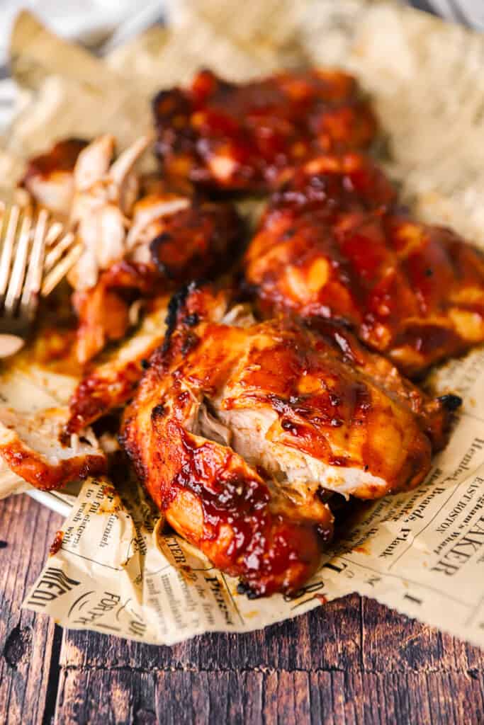 close photo of a bbq chicken thigh partially cut open on brown newsprint paper.