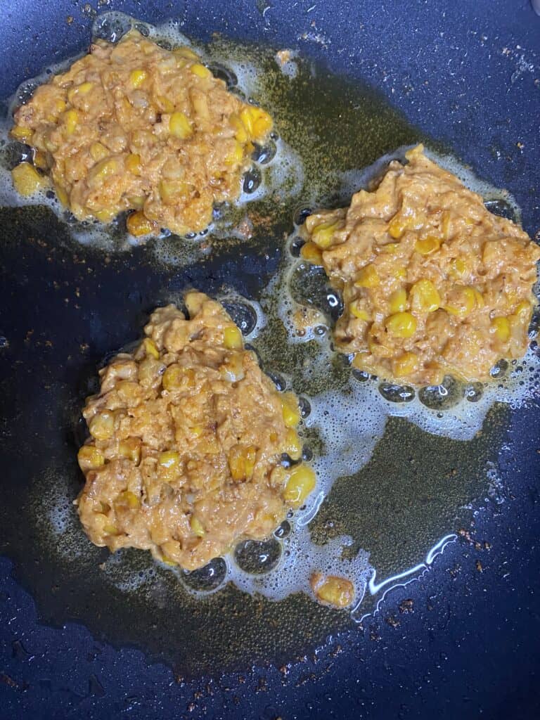 three fritters frying in the oil in a black non-stick pan.
