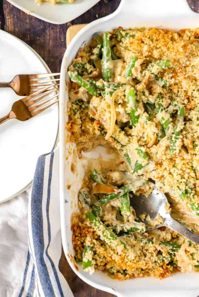 green bean casserole in a white baking dish with two copper forks 