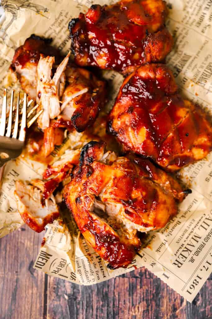 the oven baked BBQ chicken on brown newsprint paper slightly pulled apart with two forks.