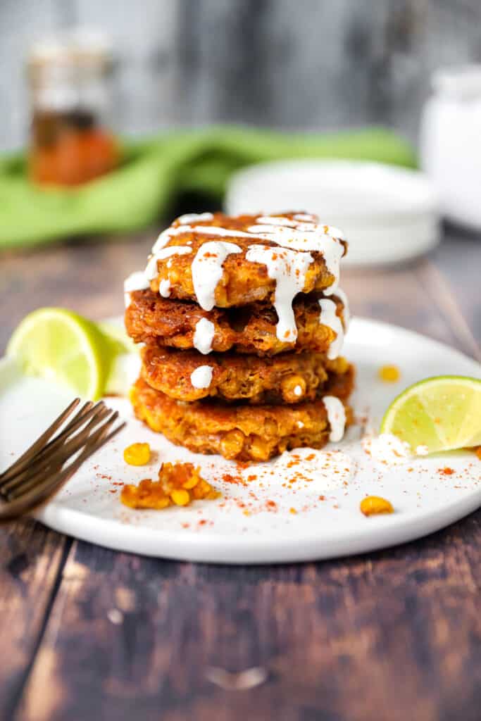 a stack of 4 spicy corn fritters drizzled with sour cream sauce on a white plate.