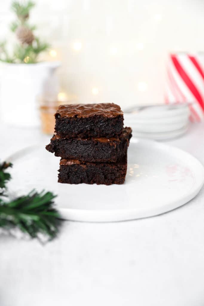 stack of 3 brownies on a white round plate, white lights in the background.