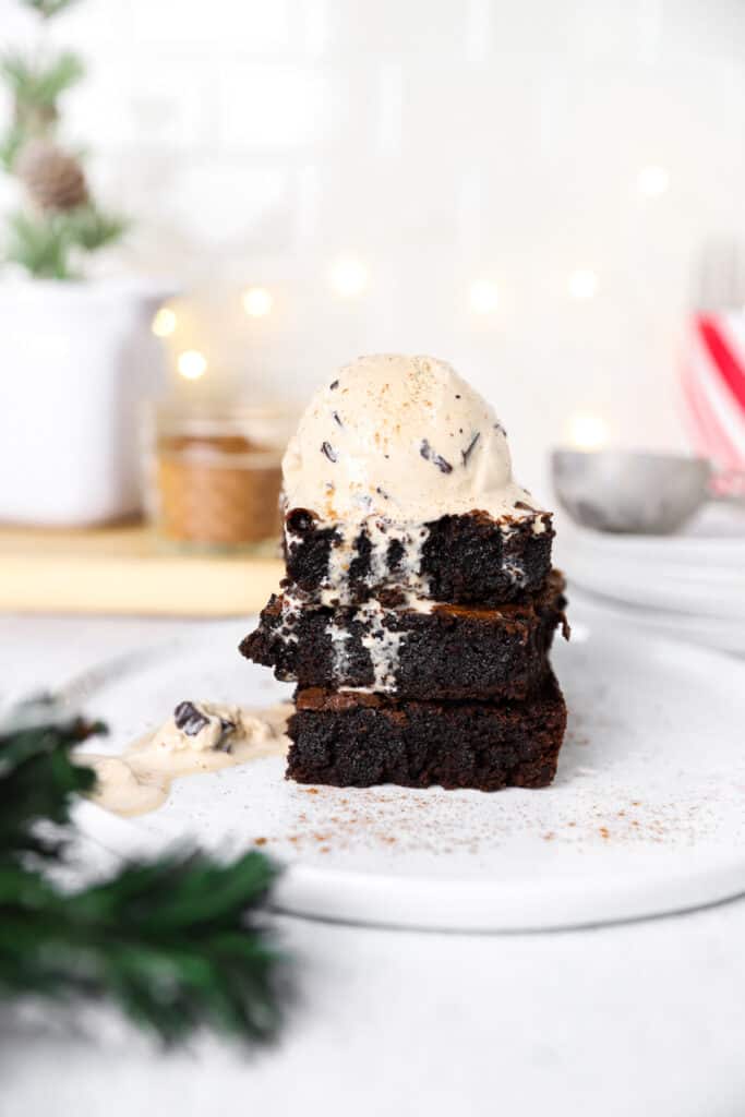 a stack of 3 brownies topped with coffee ice cream on a white round plate.