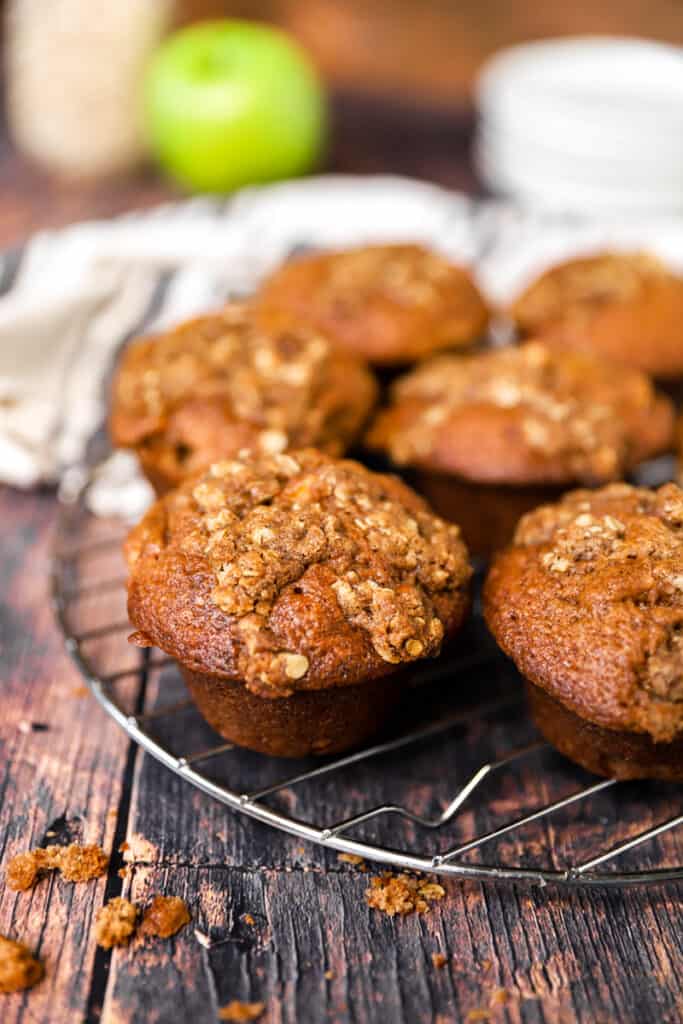 the muffins on a baking rack on a wood surface, plates and linen in the back.