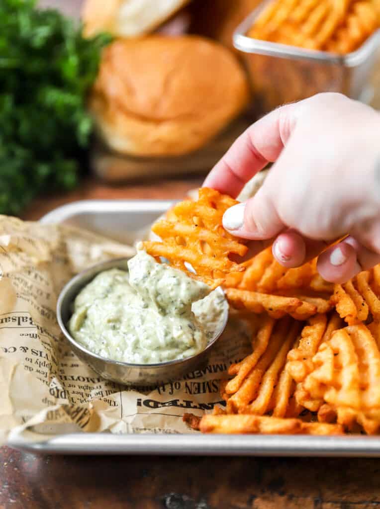 a hand dipping a waffle fry into the the pesto mayo