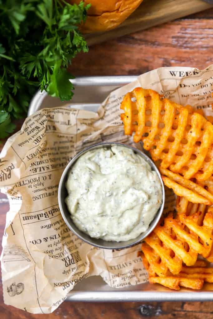 overhead shot of the pesto mayo in a small silver dish with waffle fries on brown newsprint paper.