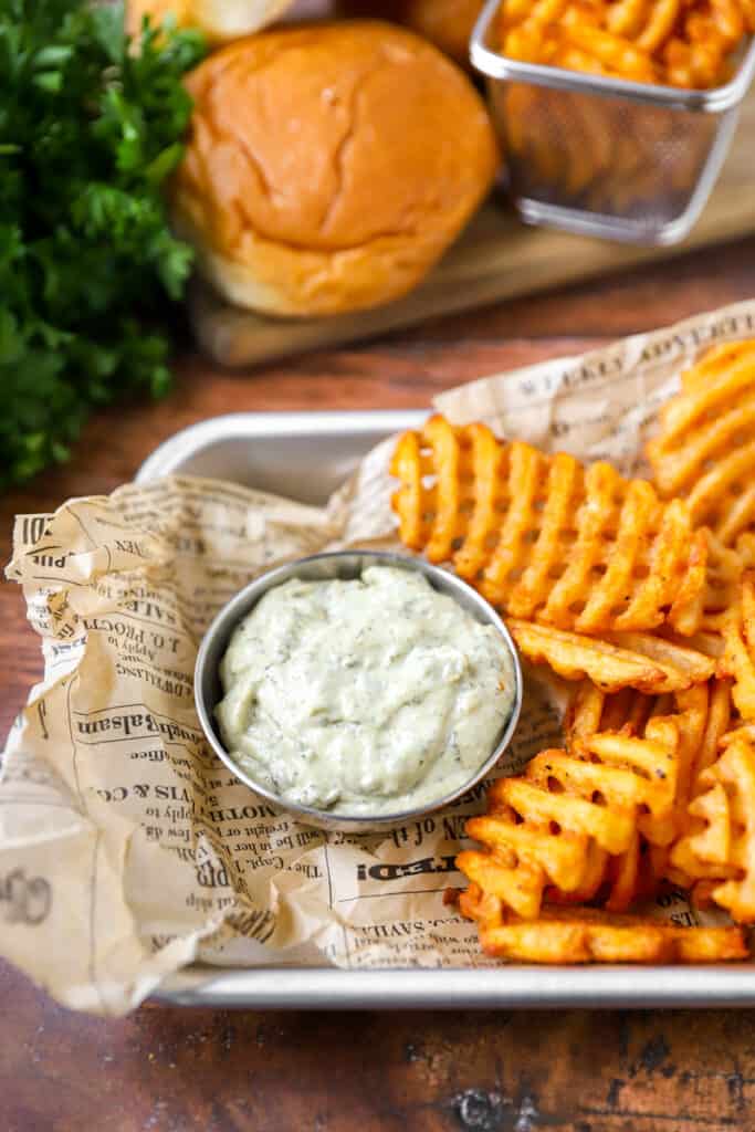 pesto mayo in a silver dish with waffle fries on brown newsprint paper.