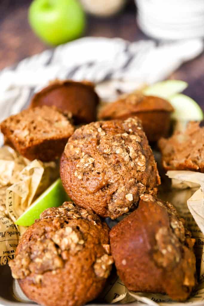 a pile of the muffins showing the streusel topping. A green apple and ivory linen in the back.