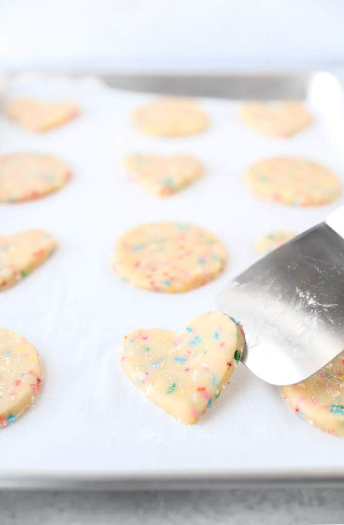 spatula adding a heart shaped cookie to the baking sheet.