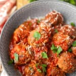 baked meatballs in a grey bowl topped with Parmesan and parsley.